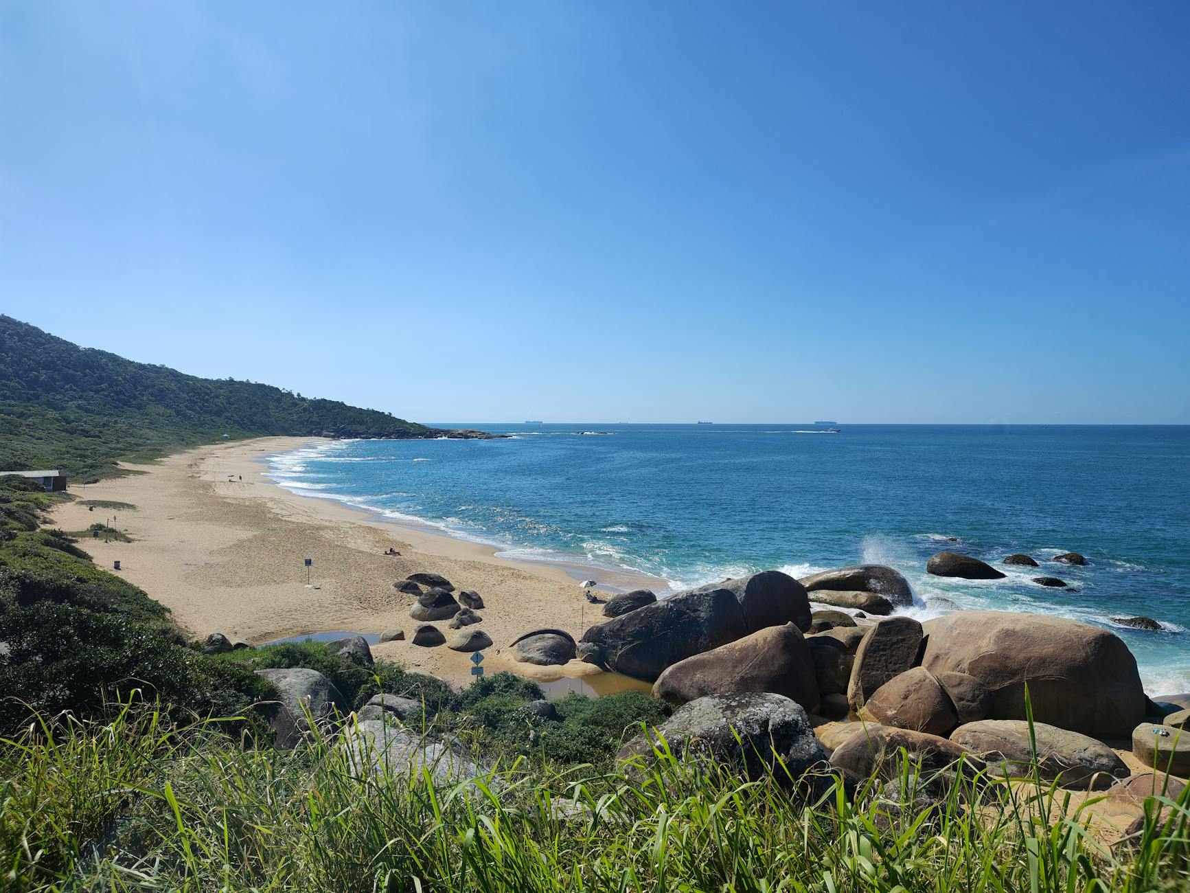 Uma vista deslumbrante da praia de Balneário Camboriú com ondas do mar e vegetação exuberante em um dia ensolarado.