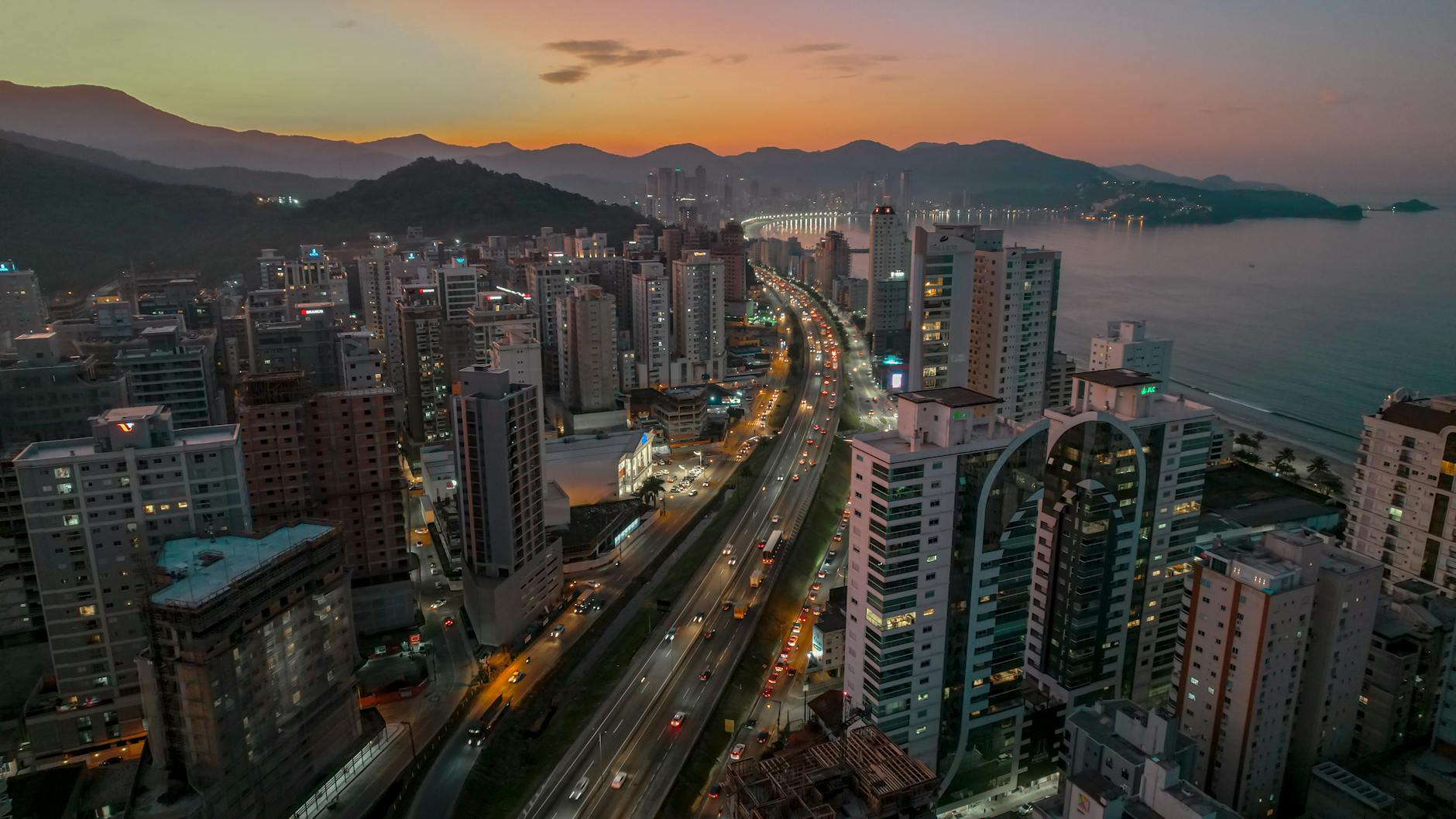 Vista aérea de Itapema, Brasil, durante o pôr do sol, mostrando as luzes da cidade e o litoral.