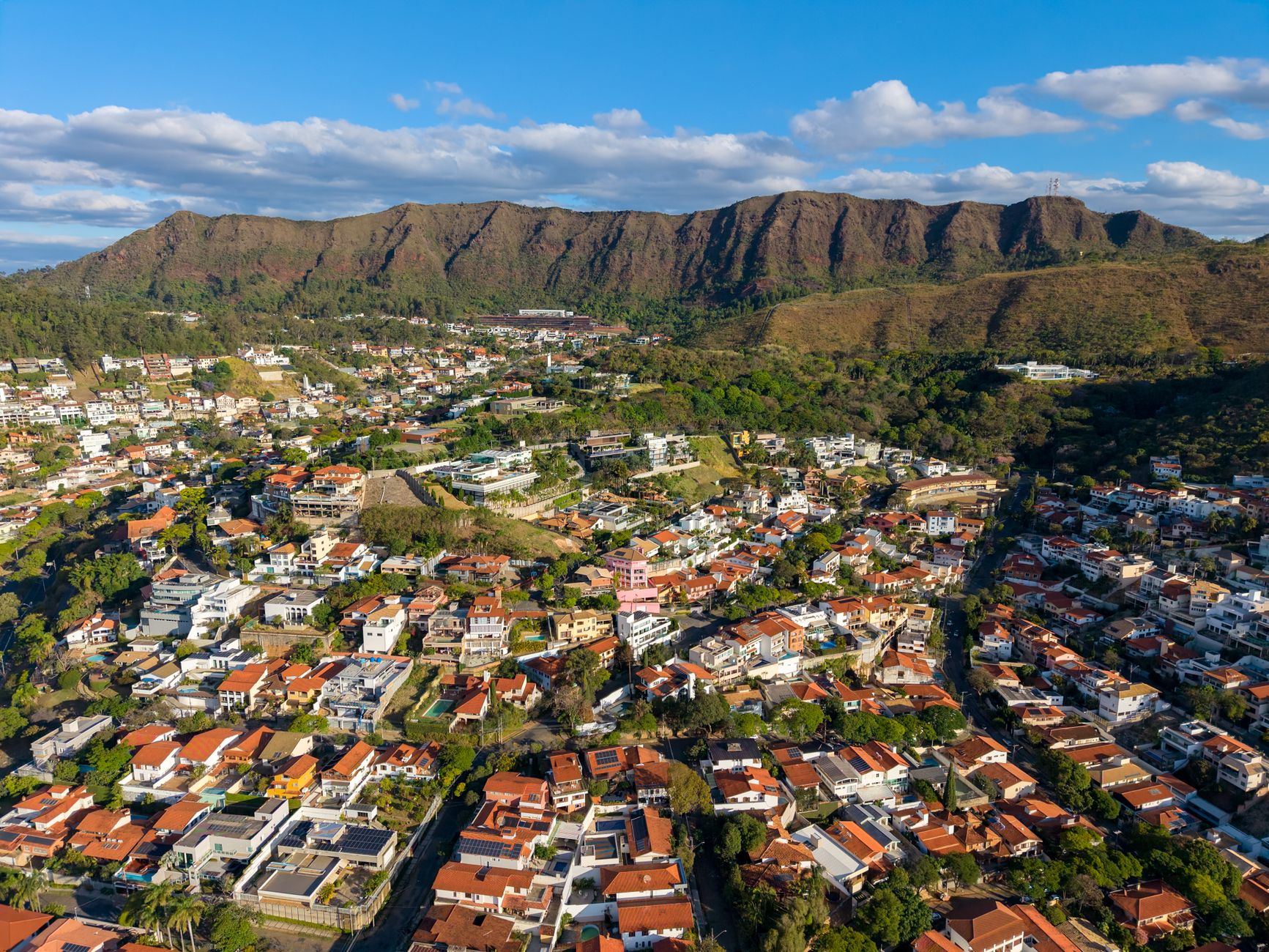 Foto aérea deslumbrante da Serra do Curral e do bairro de Belo Horizonte ao redor sob um céu azul brilhante.