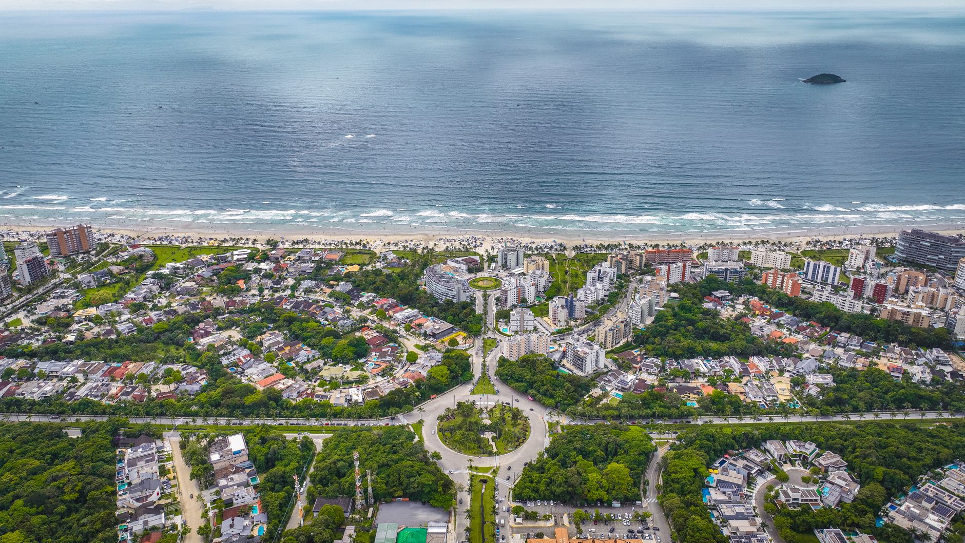 Vista aérea de uma cidade costeira com vegetação exuberante, edifícios e uma ampla praia.
