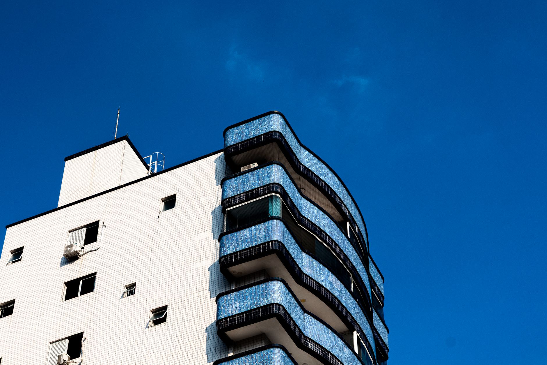 Um edifício de arquitetura moderna com varandas azuis e um céu azul límpido.