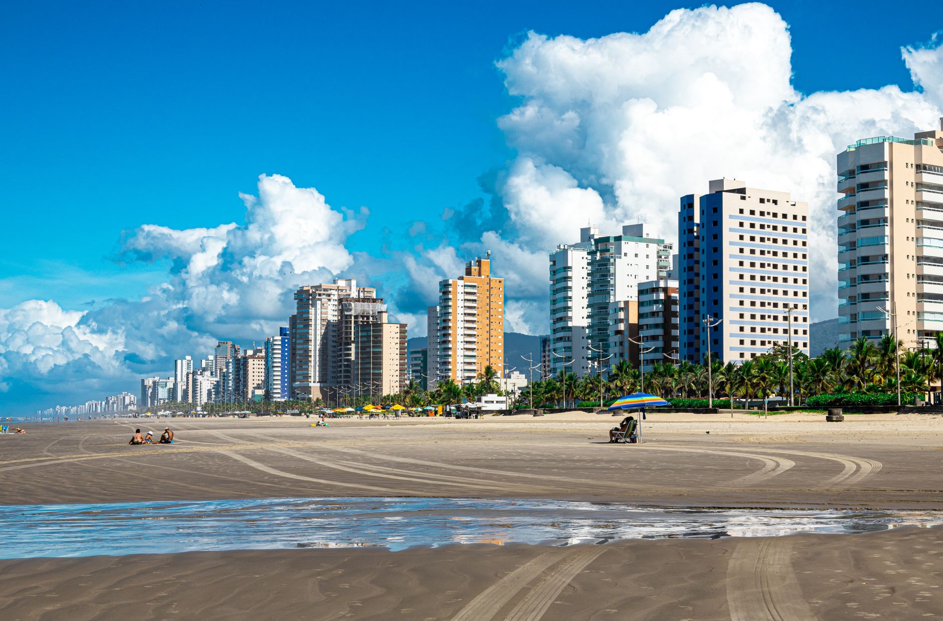 Uma vista vibrante do horizonte da Praia Grande, com apartamentos imponentes e uma praia de areia serena sob um céu azul claro.
