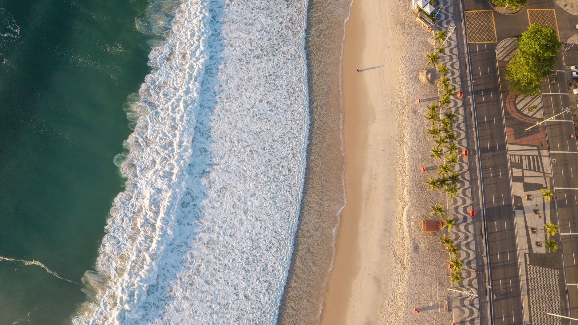 Impressionante foto aérea de uma praia do Rio de Janeiro, com a luz dourada do sol realçando as ondas e o litoral.