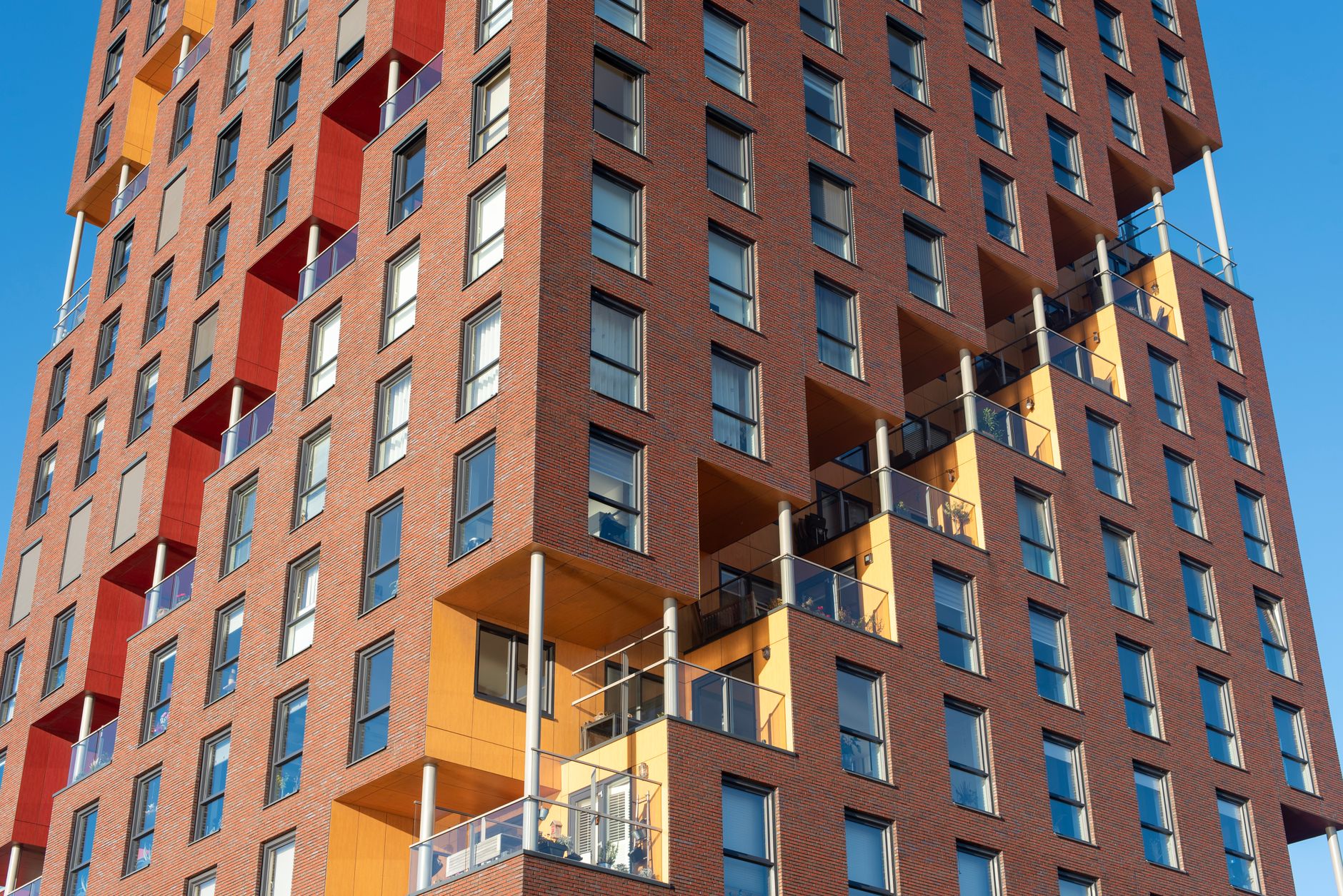 Uma fachada de edifício moderno com varandas geométricas, tijolos e elementos de design coloridos contra um céu azul claro.