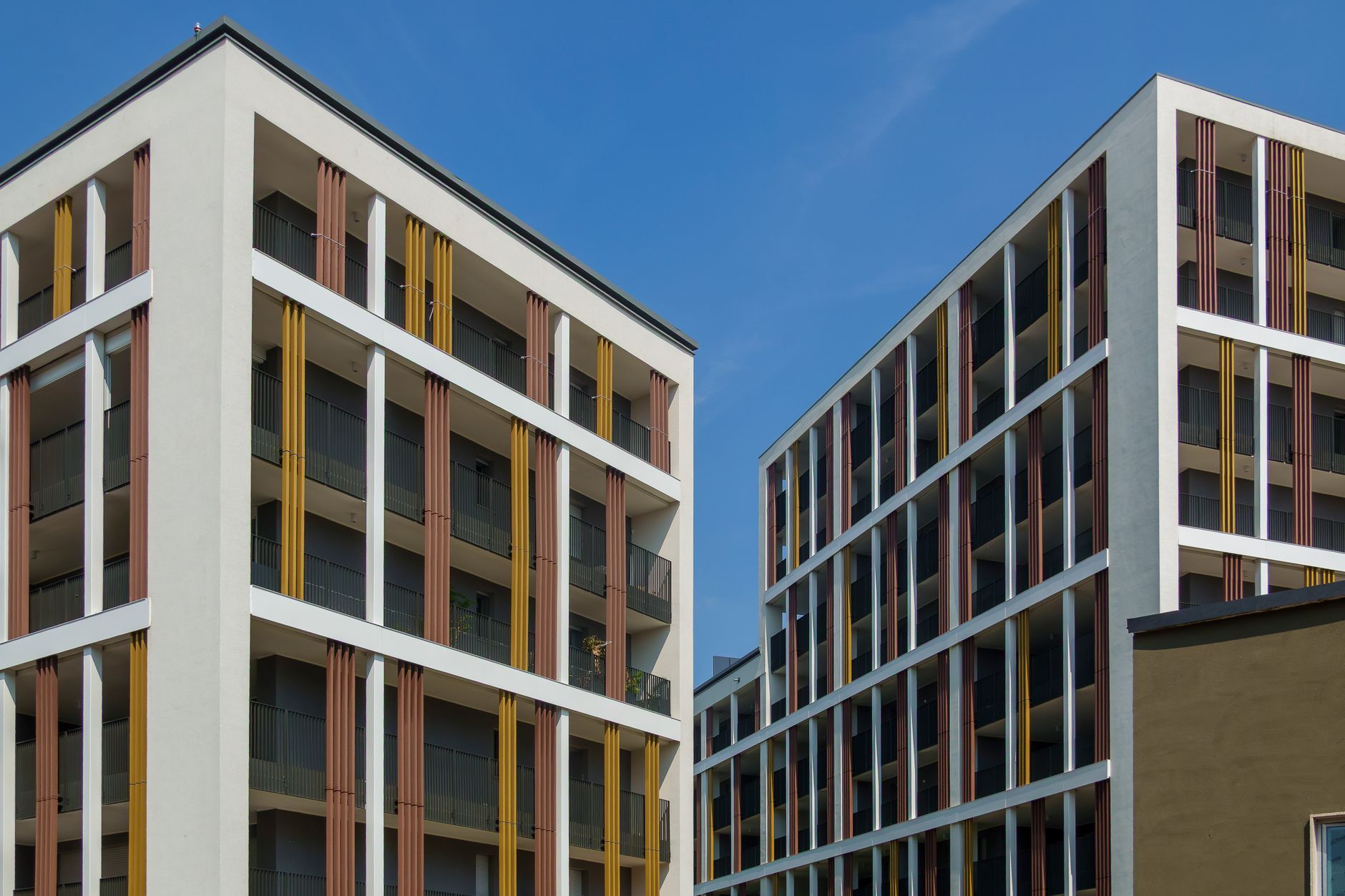 Prédios de apartamentos contemporâneos com fachadas coloridas sob um céu azul claro, exibindo arquitetura moderna.