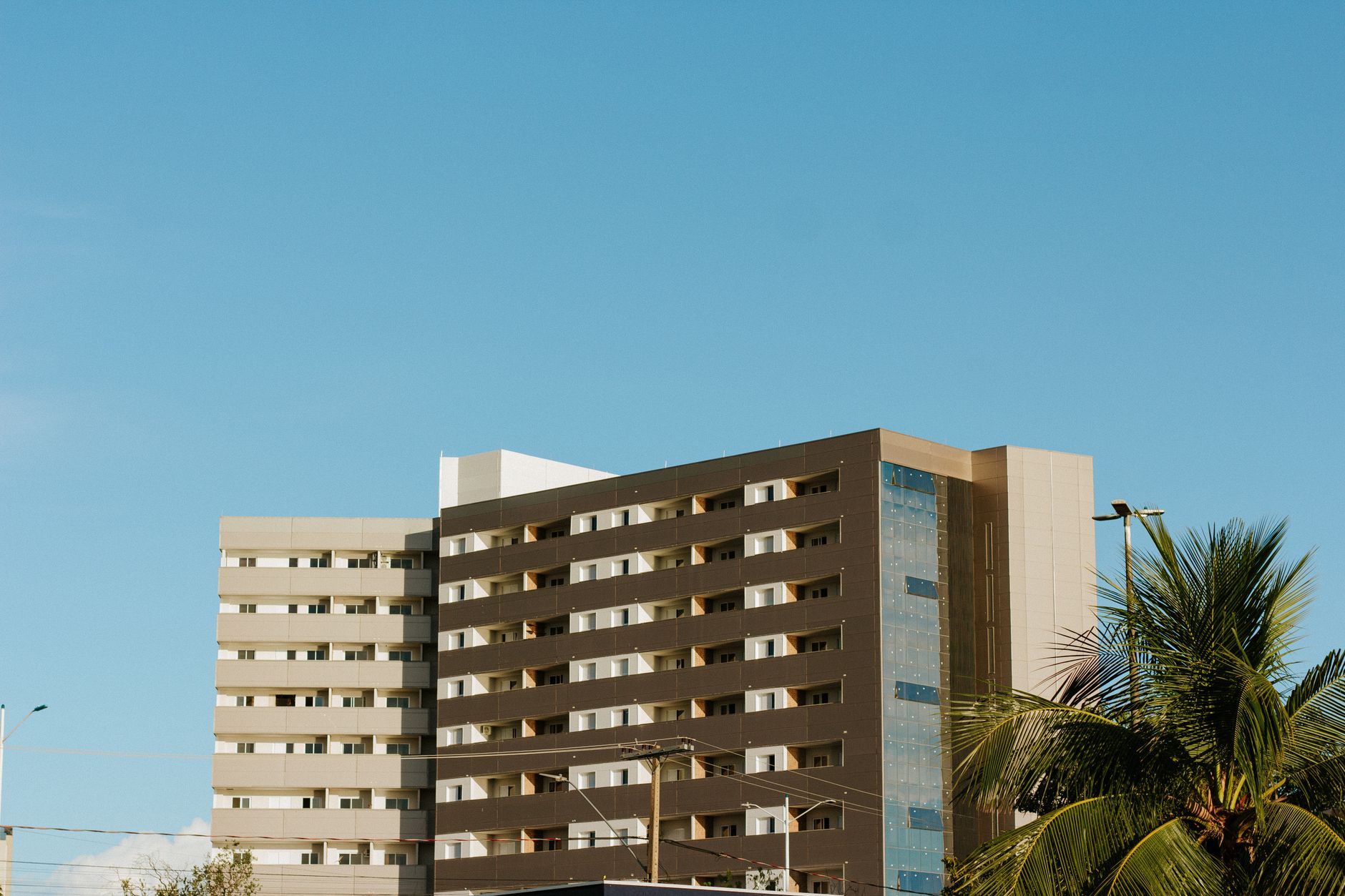 Prédio de apartamentos contemporâneo em Palmas, Brasil, com céu azul claro e palmeiras.