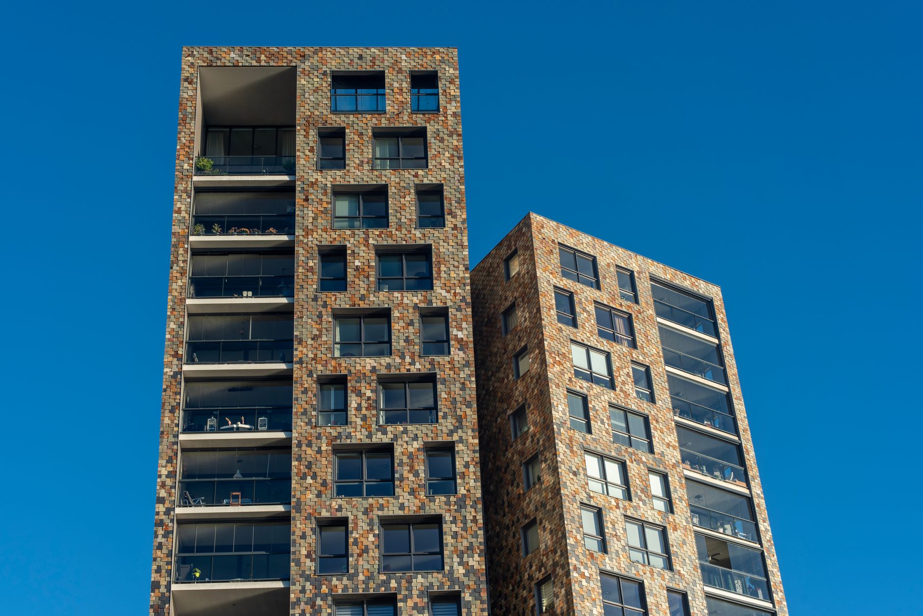 Dois edifícios altos e modernos com uma fachada de tijolos contra um céu azul claro.
