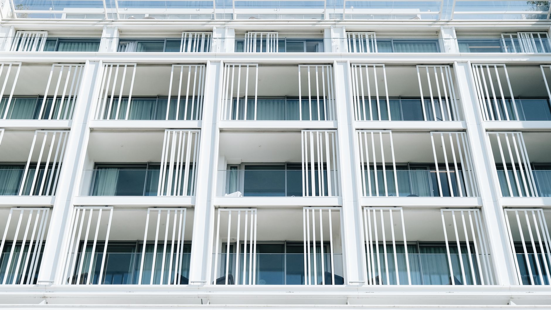 Vista aproximada da fachada de um prédio de apartamentos moderno, branco, com linhas verticais e janelas de vidro.