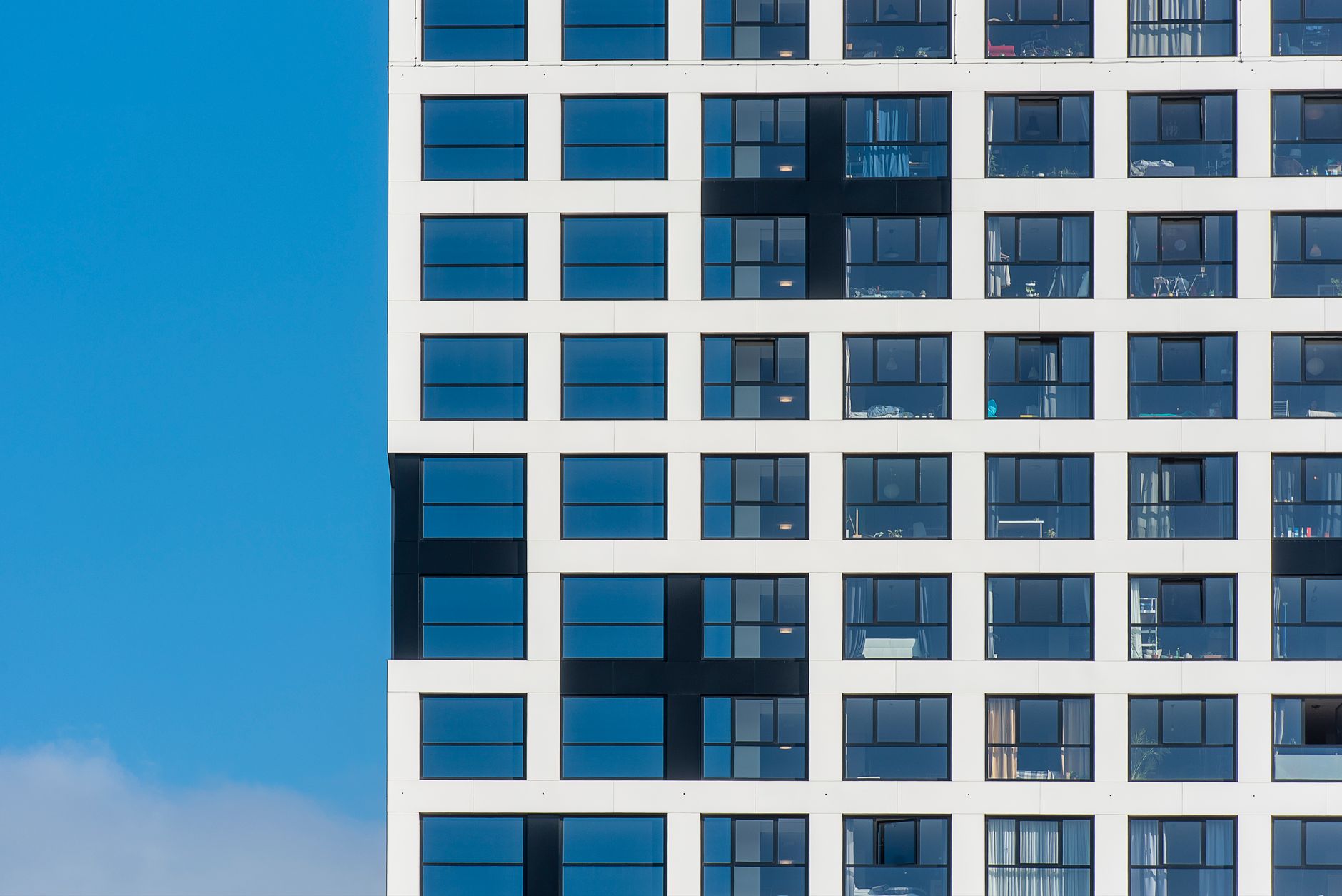 Vista de perto da fachada de um edifício moderno com janelas gradeadas contra um céu azul claro.