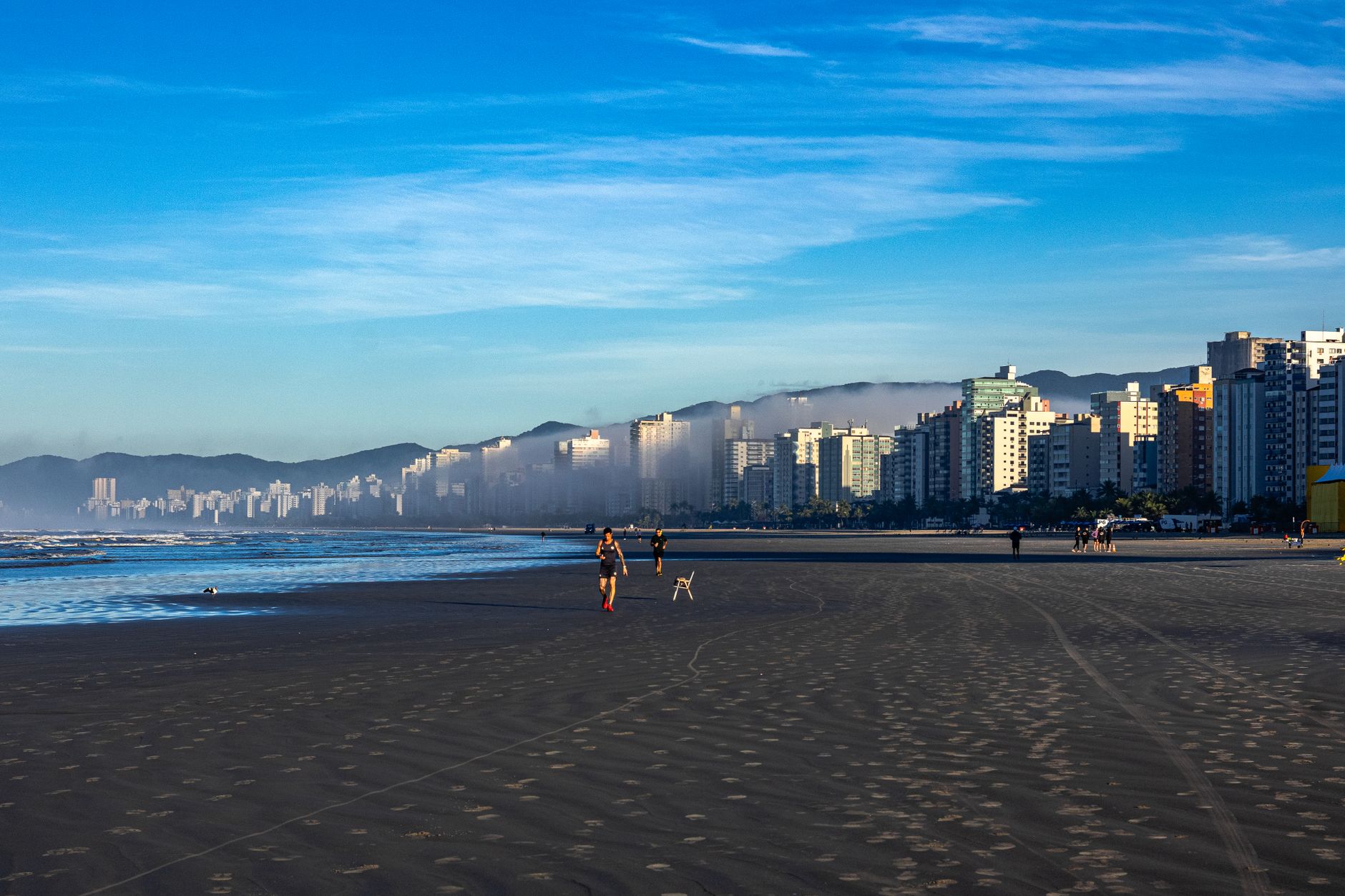 Vista matinal da orla de Praia Grande com corredores e prédios altos sob um céu azul claro.