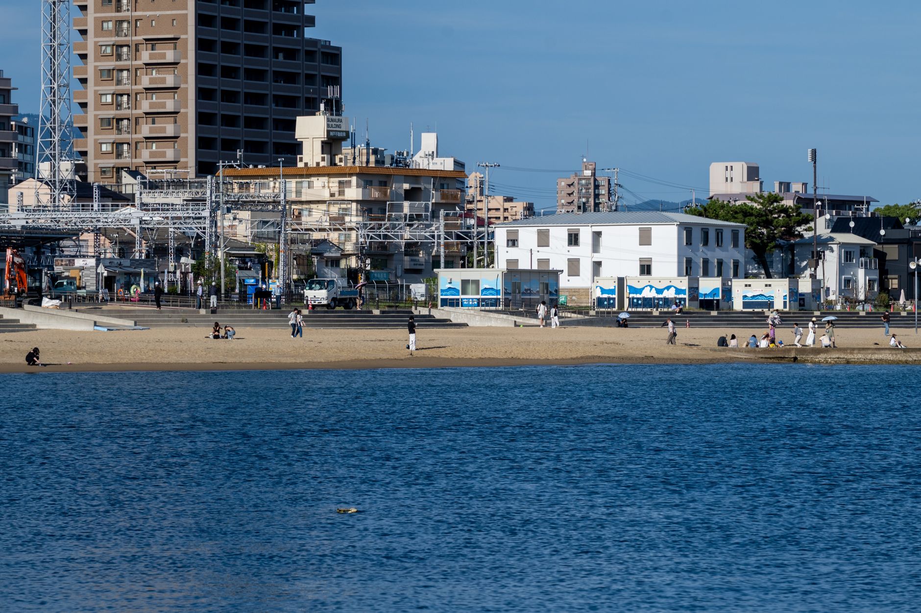Uma praia com o horizonte da cidade mostrando pessoas aproveitando um dia ensolarado na água.