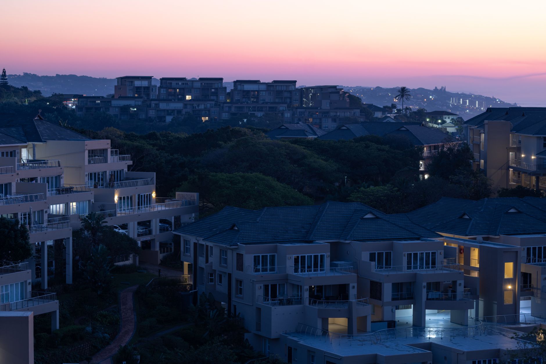 Uma paisagem urbana serena ao entardecer, com prédios de apartamentos modernos e um céu vibrante ao pôr do sol.