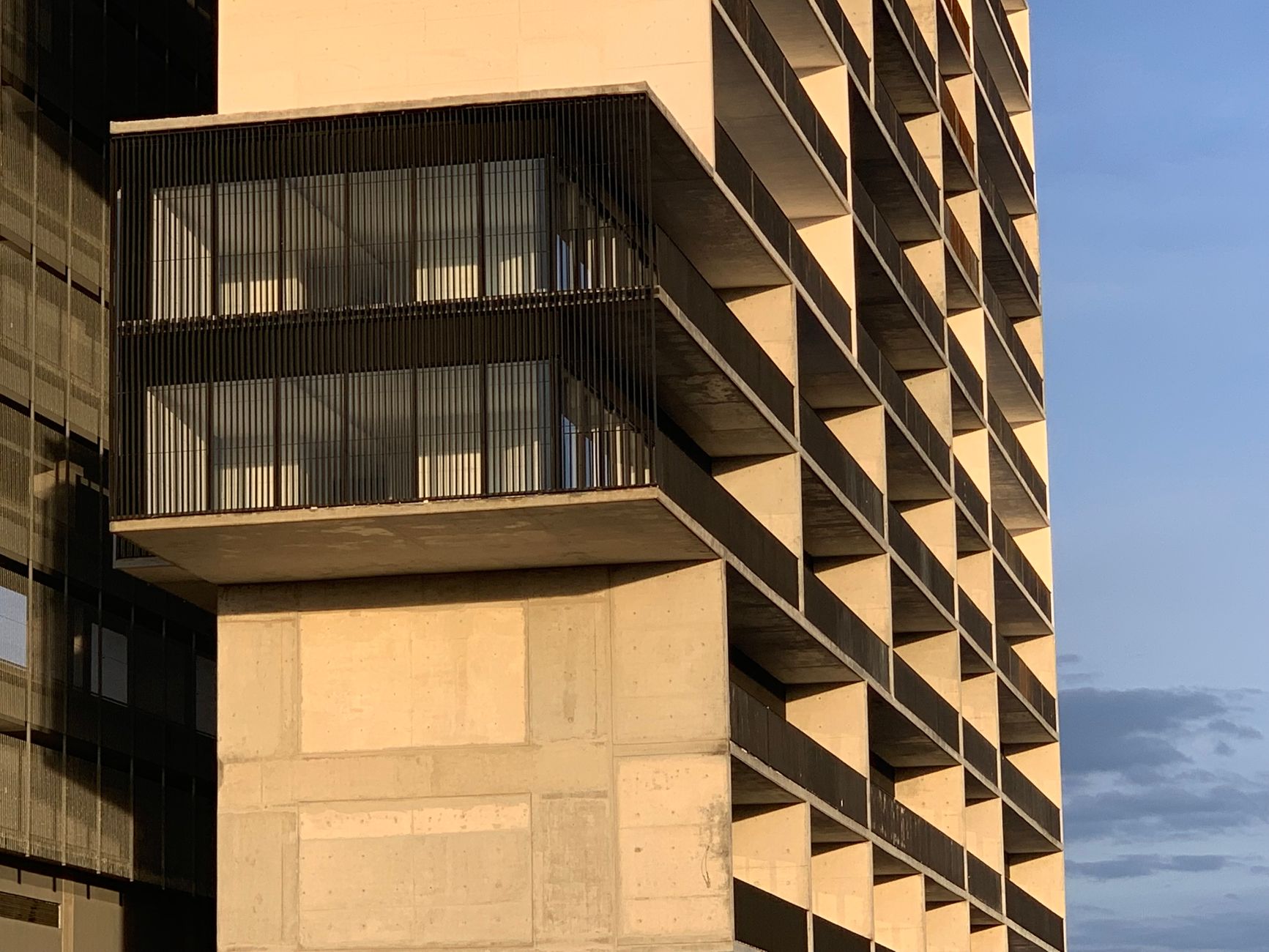 Vista do pôr do sol na fachada de um edifício brutalista moderno em Puebla, exibindo design geométrico e texturas de concreto.