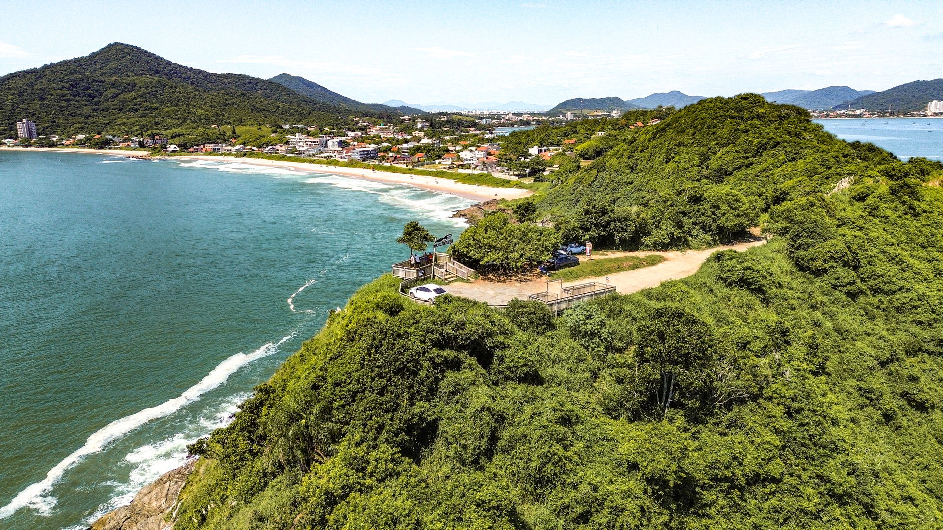 Vista aérea do litoral de Itajaí com colinas verdejantes e oceano azul sob um céu limpo.