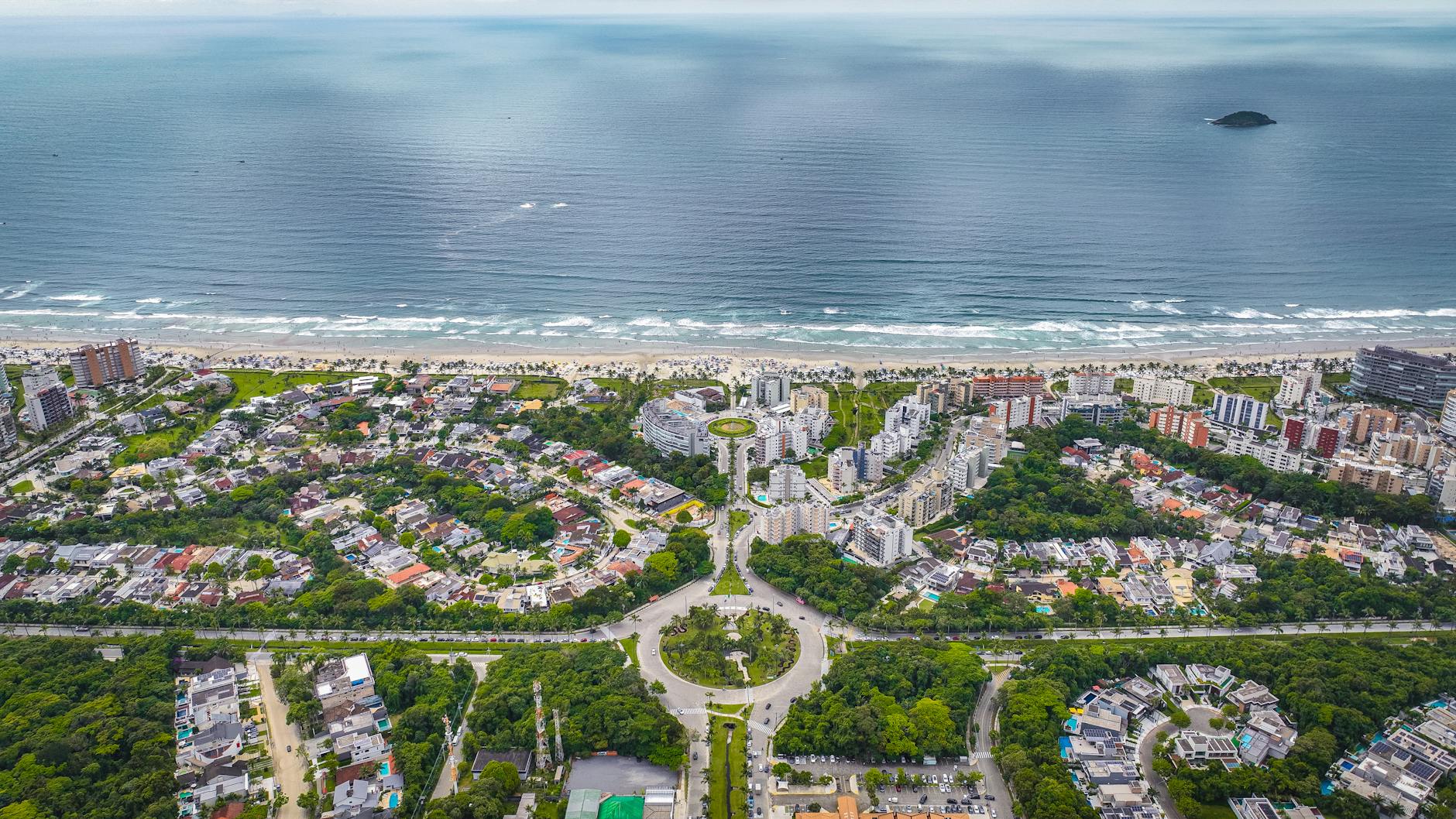 Vista aérea de uma cidade costeira com vegetação exuberante, edifícios e uma ampla praia.