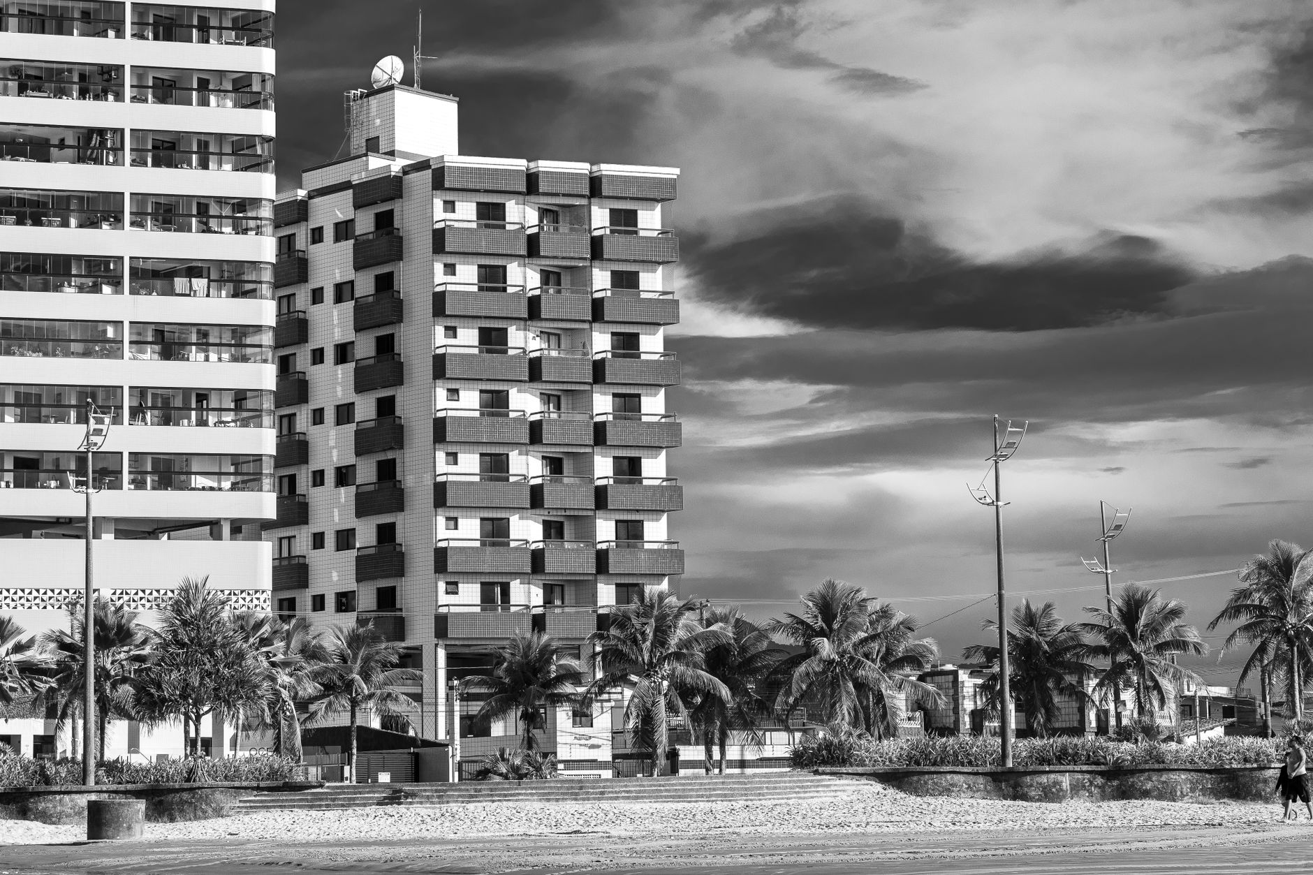 Imagem monocromática de apartamentos à beira-mar com palmeiras e céu nublado.