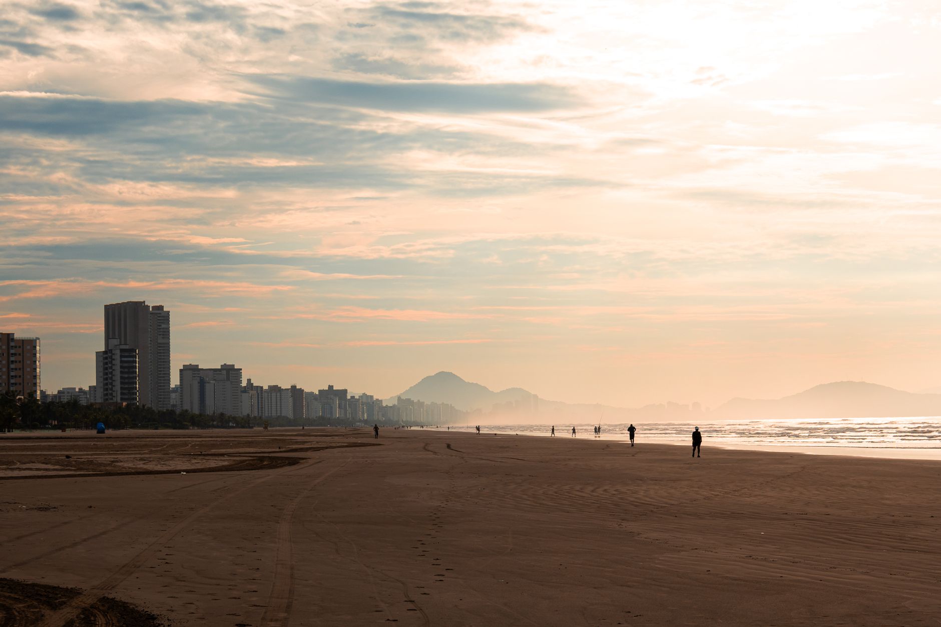 Vista panorâmica da praia de São Vicente ao entardecer, com o horizonte da cidade e as montanhas ao fundo, no Brasil.