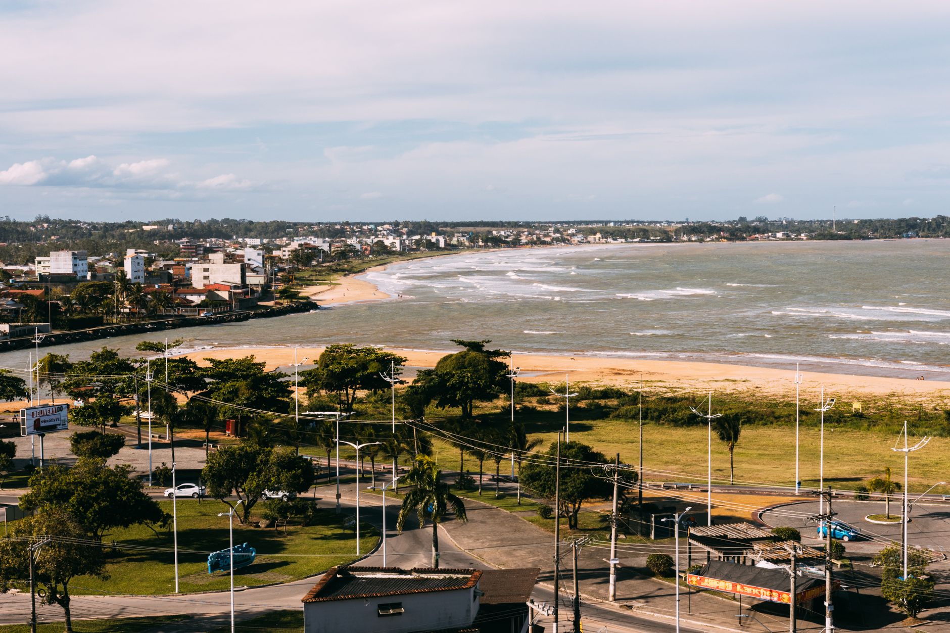 Vista aérea de uma cidade costeira com praia, oceano e edifícios modernos em um dia ensolarado.